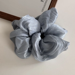 Close-up of a light blue pearlescent satin hair scrunchie with detailed soft pleats