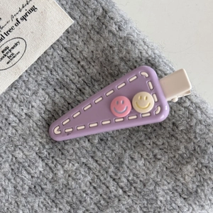 Detail of purple triangle hair clip with white stitching and cute smiley face accents