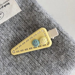 Close-up of yellow triangle hair clip with cute 3D smiling faces and stitch texture