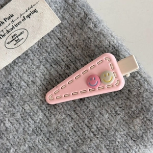 Detail of pink triangle hair clip with cute smiley faces on grey knitted background