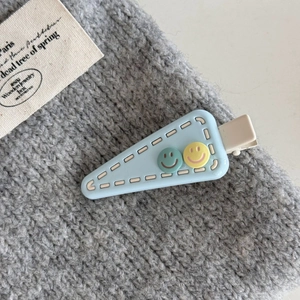 Detail of light blue triangle hair clip with cute smiley faces and duckbill design