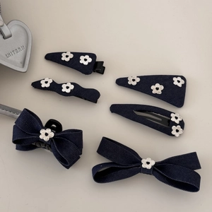 Détail de barrettes nœuds en denim bleu avec boutons fleurs argentés sur fond clair neutre