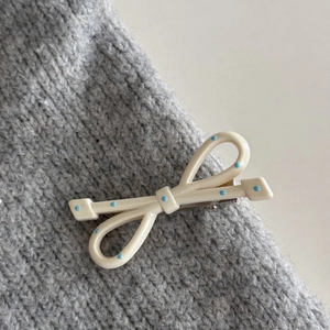 Dettaglio del fermaglio per capelli a fiocco crema con pois blu su maglia grigia