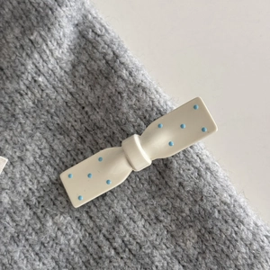 Dettaglio di un fermaglio per capelli a fiocco bianco con pois blu su maglia grigia