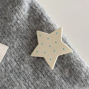 Primo piano di un fermaglio a stella color crema a pois blu su tessuto a maglia grigio