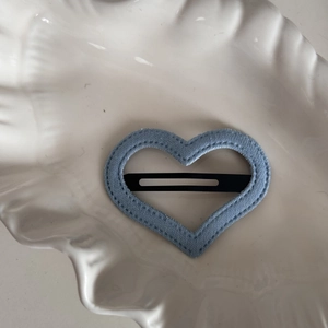 Detail of heart-shaped blue denim fabric hair clip with stitching on beige ceramic plate