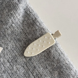 Dettaglio macro di un fermaglio crema con micro perline su tessuto in maglia grigia