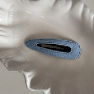 Close-up of light blue denim fabric BB hair clip with decorative stitching on white ceramic tray
