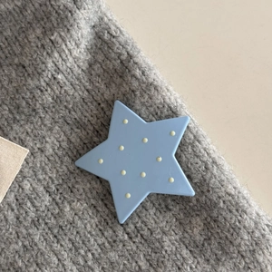 Macro di una molletta a stella azzurra a pois gialli su un maglione grigio lavorato