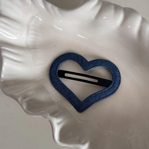 Close-up of denim fabric heart hair clip resting on a white shell plate decoration
