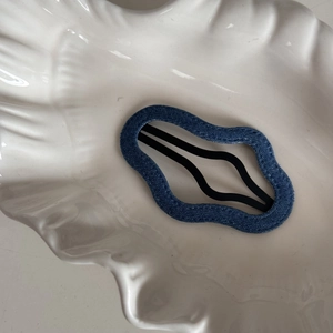 Close-up of denim fabric wavy BB hair clip with black metal base on a shell tray