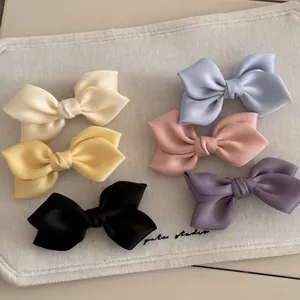 Set of six colorful satin bow hair clips in pastel tones on a neutral fabric background