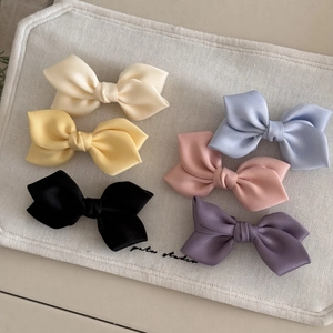 Close-up of colorful satin bow hair clips in cream, yellow, pink, and blue on linen