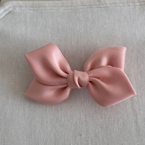 Close-up of a soft pink satin bow hair clip with smooth texture and knotted center