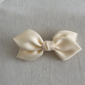 Detailed macro view of a creamy ivory satin ribbon hair bow with smooth silky texture