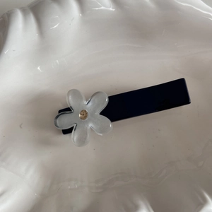 Dettaglio di un fermaglio blu con fiore opaco traslucido e un piccolo cristallo ambrato