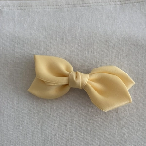 Close-up of pale yellow satin ribbon bow hair clip with glossy texture and elegant design