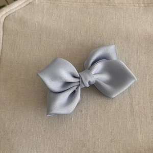 Detailed view of light blue satin bow hair clip with smooth silk texture on linen