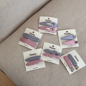 Dettaglio di fermagli per capelli in tessuto a pois rosa e blu su un cartoncino bianco