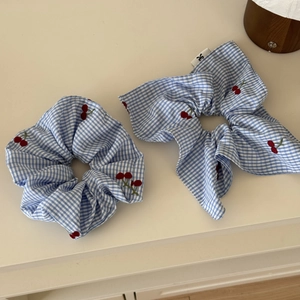 Detailed view of blue checkered scrunchie with red cherry embroidery and bow