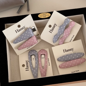 Dettaglio di fermagli per capelli a pois rosa e blu esposti su cartoncini fatti a mano