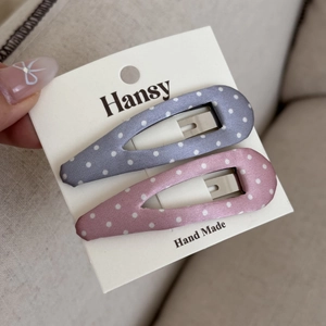 Dettaglio di fermagli per capelli a pois rosa e blu su un cartoncino bianco di marca