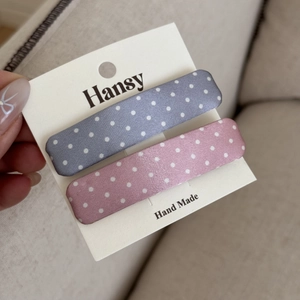 Dettaglio di fermagli per capelli a pois rosa e blu presentati su un cartoncino bianco