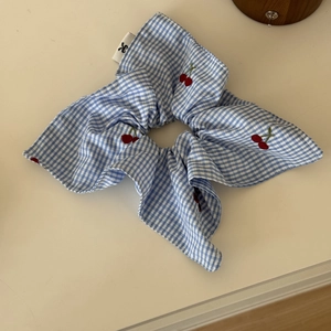 Detail view of blue checkered scrunchie with red cherry embroidery and white brand label