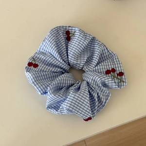 Close-up of blue gingham hair scrunchie featuring detailed red cherry embroidery texture