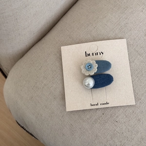 Détail de barrettes à nœuds en tissu bleu avec perle et fleur sur support cartonné