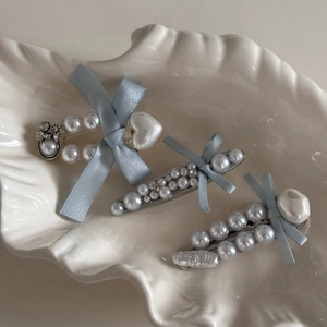 Elegant blue bow hair clips set with pearls and rhinestones on a white shell plate