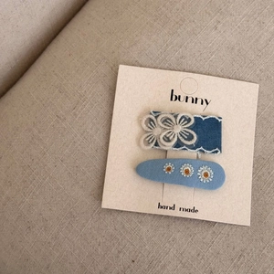 Détail de deux barrettes en tissu bleu avec fleurs en dentelle et broderie marguerite
