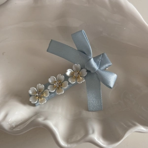 Close-up of light blue ribbon bow hair clip with three white pearl flowers and rhinestones