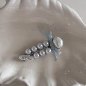 Detail view of pearl bow hair clip with blue silk ribbon on a white shell plate