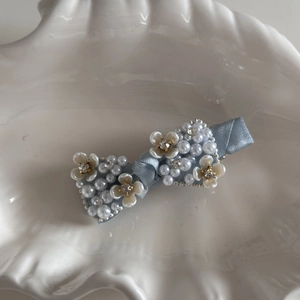 Detailed view of light blue bow hair clip with white pearls and sparkling rhinestones