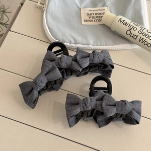Detail of grey bow hair clips in two sizes on a white wooden surface for styling