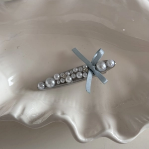 Detail of pearl bow hair clip with rhinestones and light blue silk ribbon in a shell tray