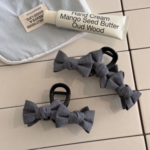 Close-up of two dark grey bow hair claws featuring textured fabric on beige tile surface