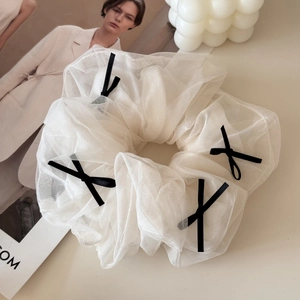 Macro detail of white mesh scrunchie with four black ribbon bows on beige background