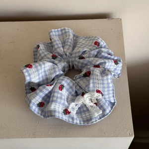 Close-up of blue plaid scrunchie with strawberry embroidery and white lace bow detail