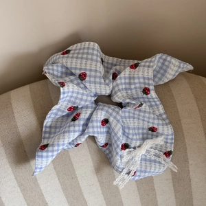 Close-up of blue plaid scrunchie with strawberry print and delicate white lace bow detail