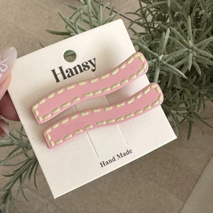 Detailed view of pink wavy hair clips with yellow stitching on a display card