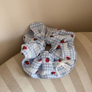 Close-up of blue plaid scrunchie with red strawberry print and white lace bow detail