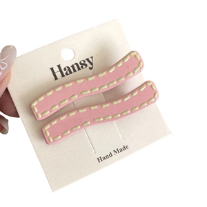 Matte pink wave-shaped hair clips set with cream stitch detail on display card