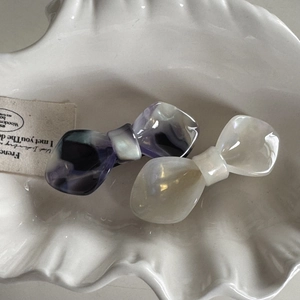 Elegant acetate bow hair clips in marble blue and pearl white on a shell dish