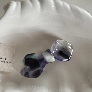 Detail view of purple marbled acetate bow hair clip placed inside a white decorative shell