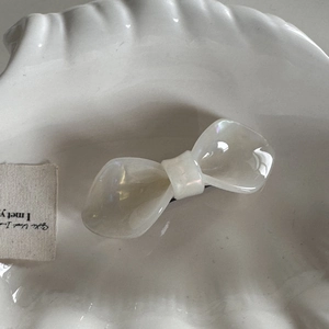 Macro shot of cream bow hair clip with pearlescent acetate finish in a shell tray
