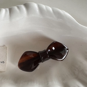 Detail of elegant dark brown acetate bow hair clip resting on a white ceramic plate