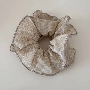 Detail of checkered chiffon scrunchie with beige plaid pattern and grey stitched edges