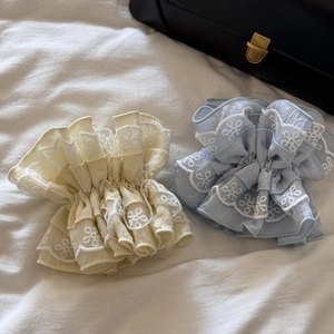Detail view of two lace scrunchies in cream white and light blue with floral embroidery